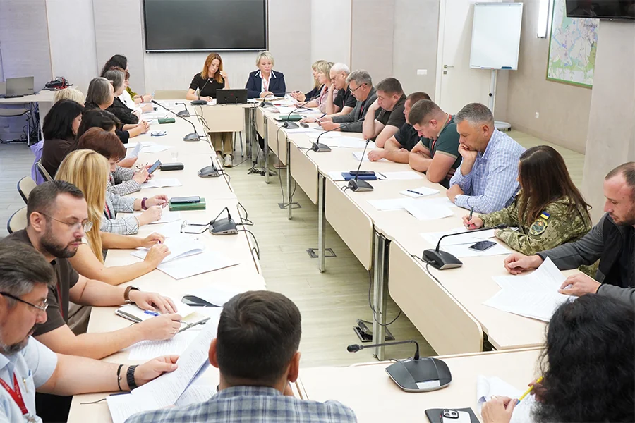 Учасники офіційного засідання сидять за столами з мікрофонами та документами